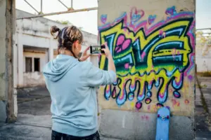 A blond woman taking a picture of graffiti at an abandoned building.