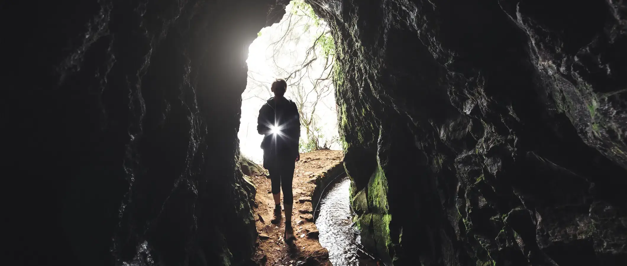 A person with a flashlight about to enter a dark cave.