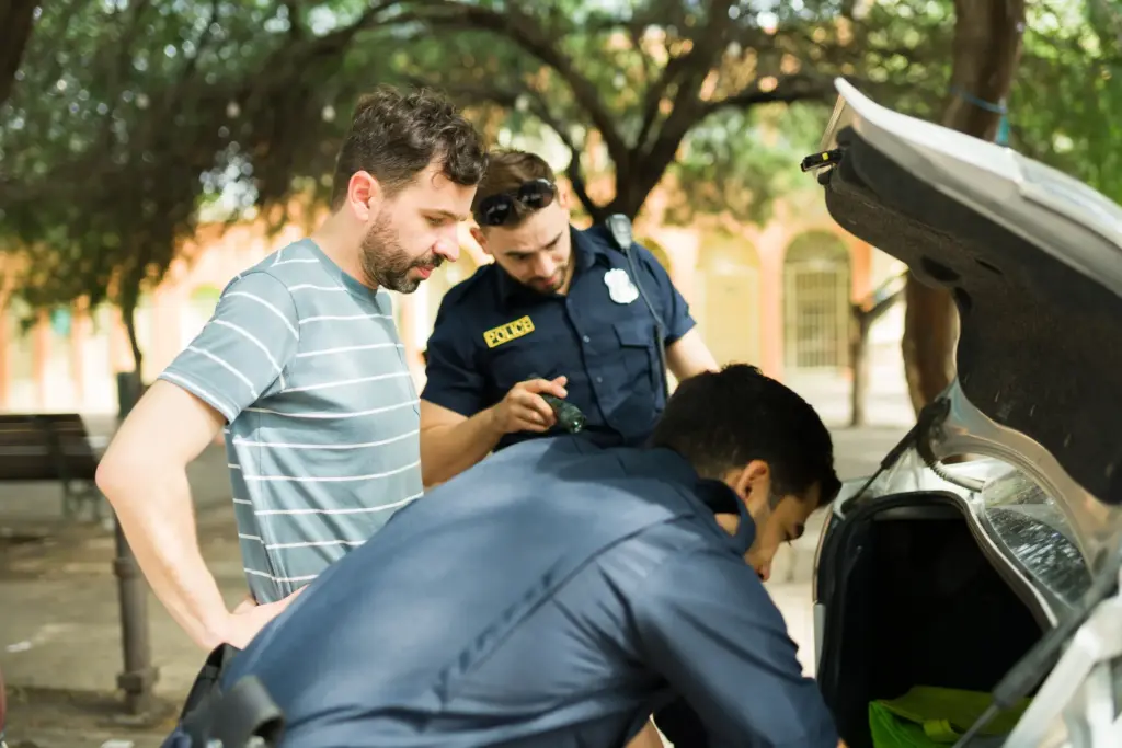 Two officers going through a man's car trunk.