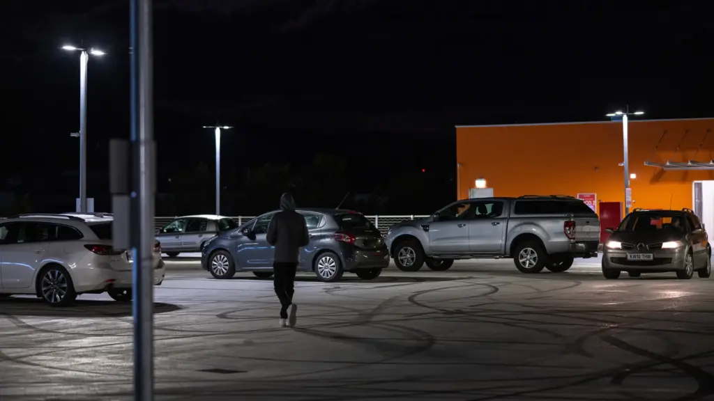 A hooded person walking in a parking lot at night. 