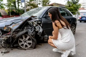 A woman looking at her car with wrecked hood.
