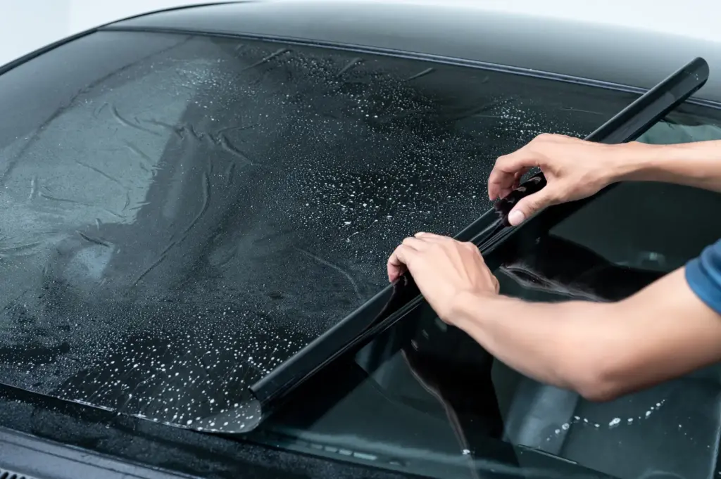 A person putting on a dark window tint on a car.