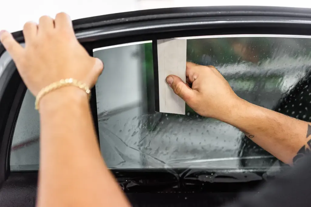 A person applying a light window tint on a car window.