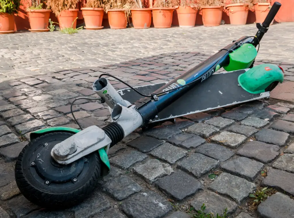 A broken electric scooter on the sidewalk.