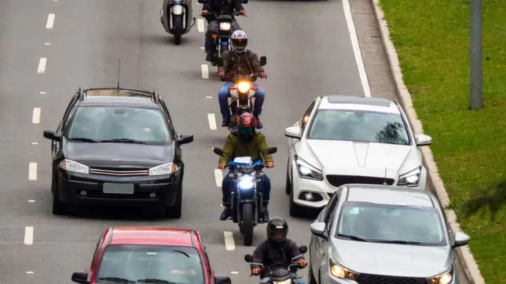 A row of motorcycles lane filtering on a busy freeway.