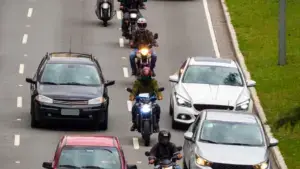 A row of motorcycles lane filtering on a busy freeway.