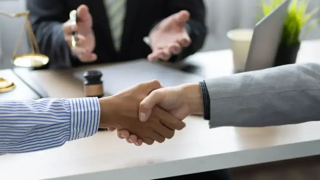 Dos personas se dan la mano mientras una persona en la parte de atrás facilita.