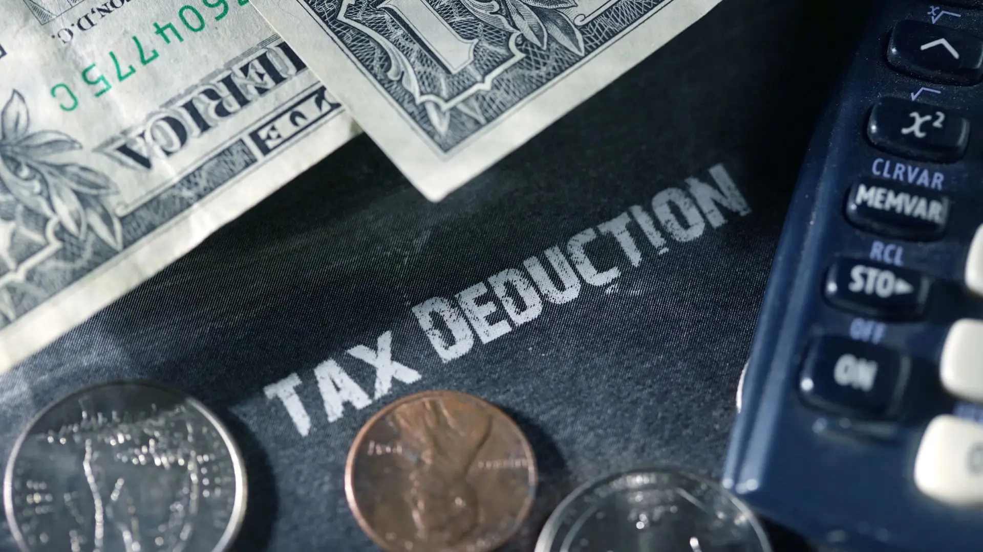 Una carpeta de deducción de impuestos con dinero y una calculadora encima.