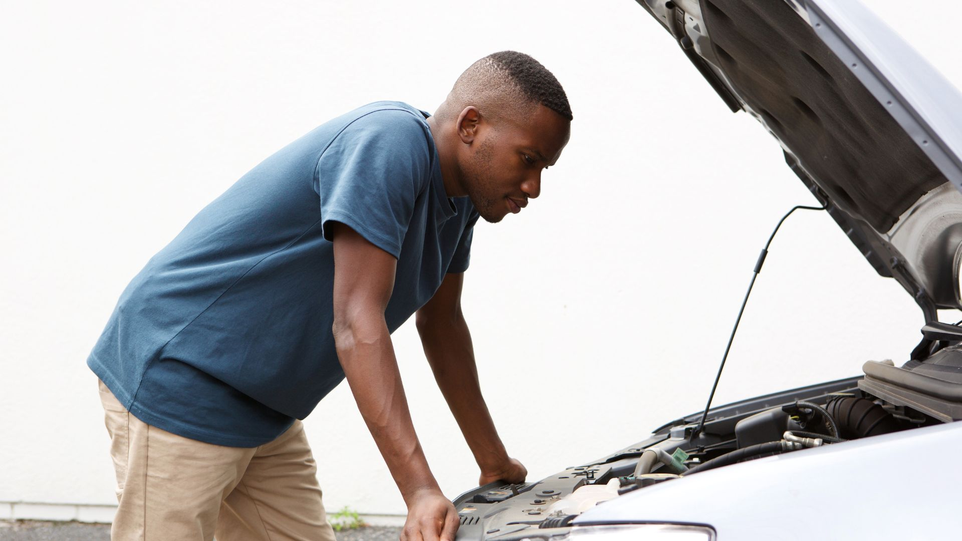 A man looking at his car engine, confused.
