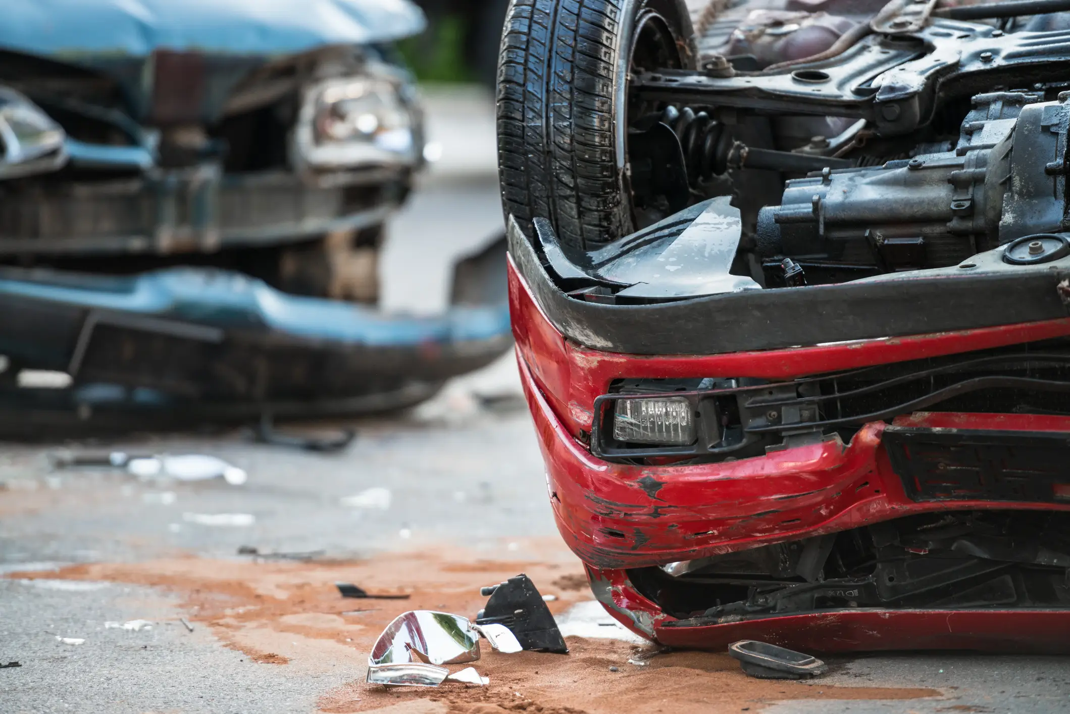 A serious car crash where a red car is upside down and a blue car is wrecked. 