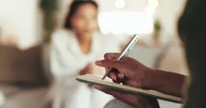A woman talking to a therapist while they are taking notes.
