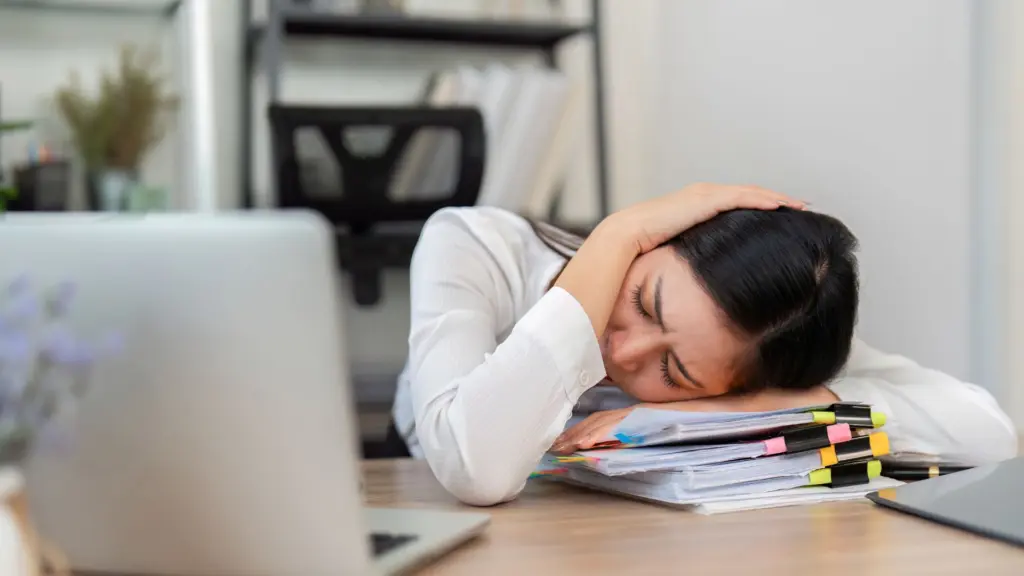 A woman holding her head in pain as she lays it on the table.
