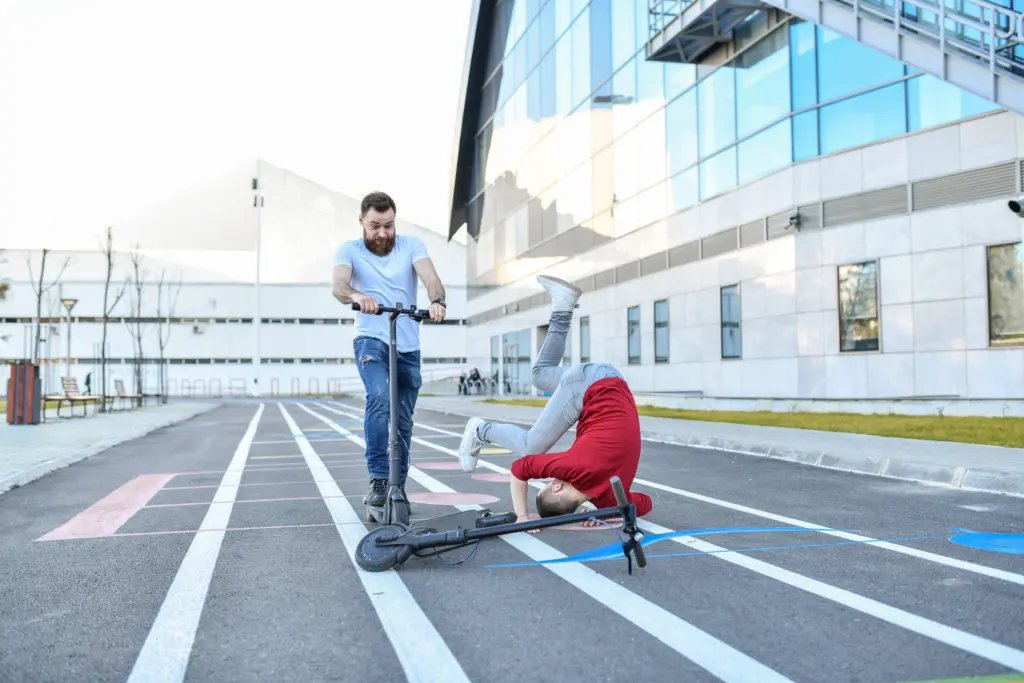 A electric scooter rider falling on his head while another riders watches in shock.
