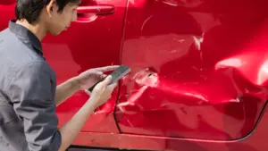 A man examining a side swiping accident on his red car.