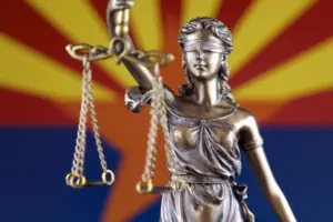 A statue of Lady Justice in front of the Arizona state flag.