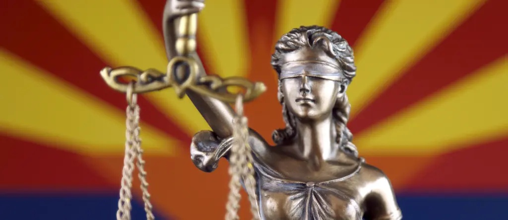 A statue of Lady Justice in front of the Arizona state flag.
