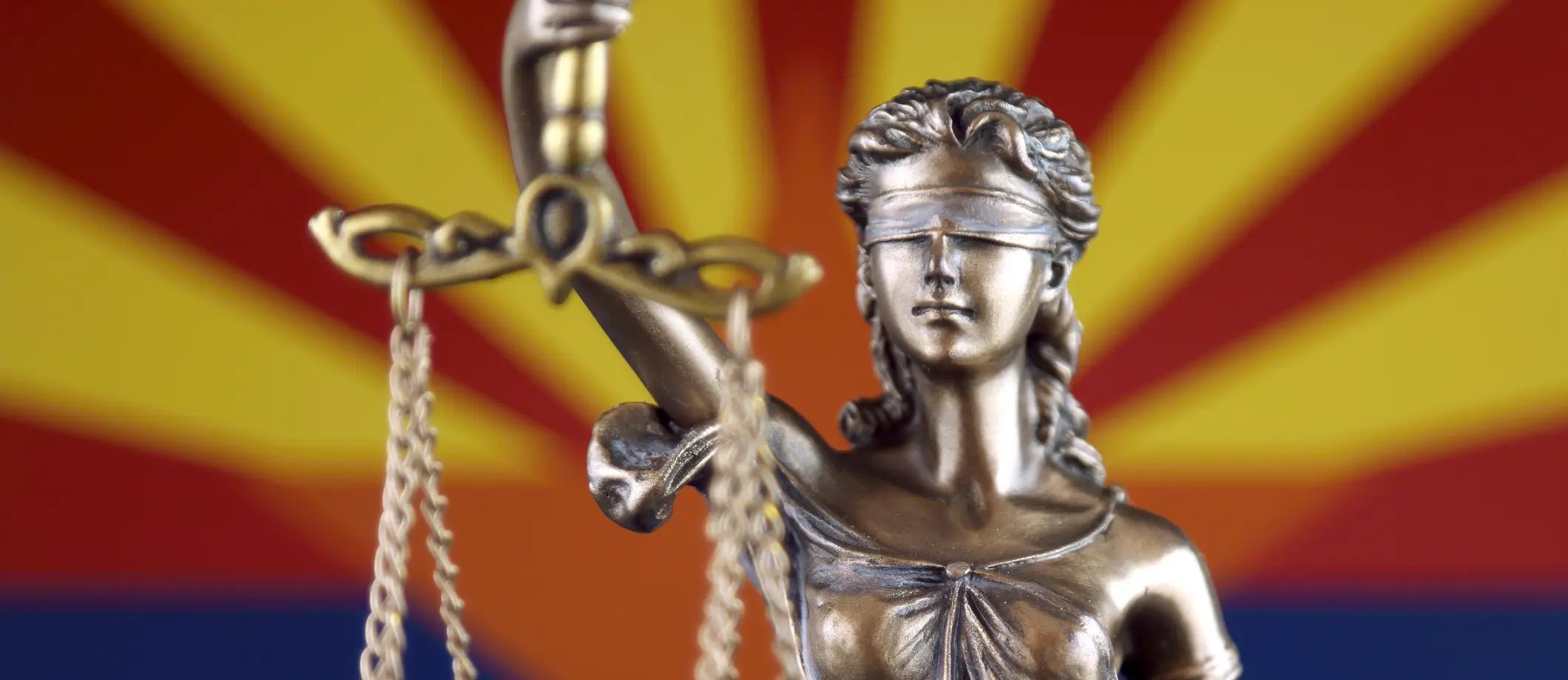A statue of Lady Justice in front of the Arizona state flag.