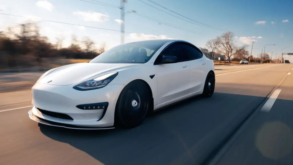 A white tesla driving on a freeway.