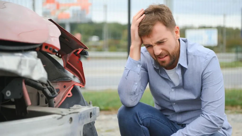 A man holding his head after looking at the damage at his car.