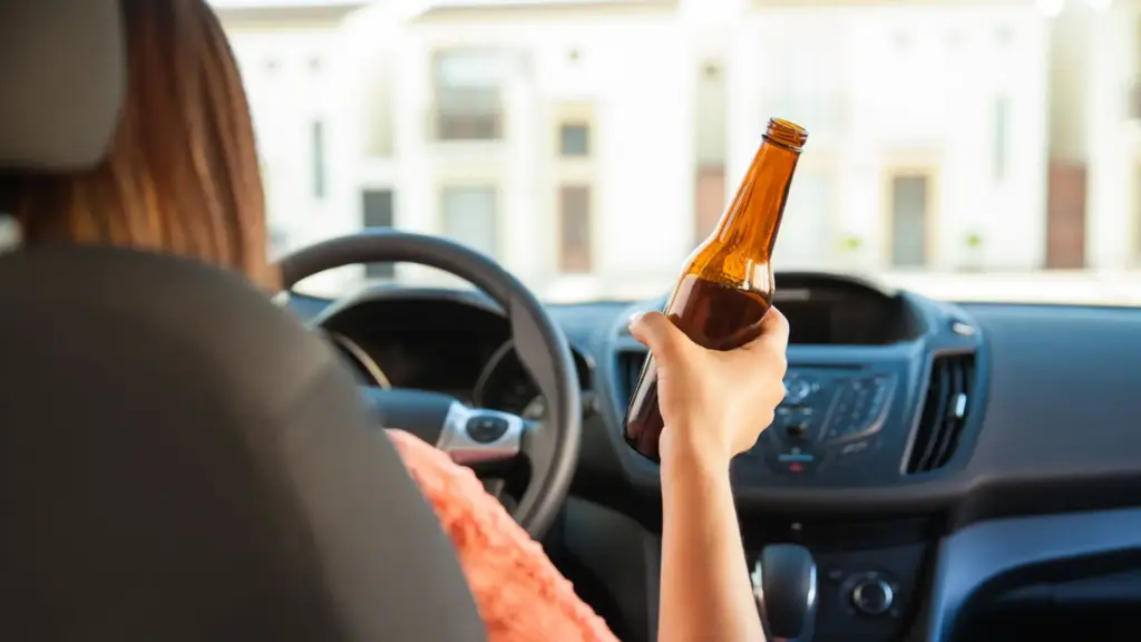 A person driving while holding a beer bottle.