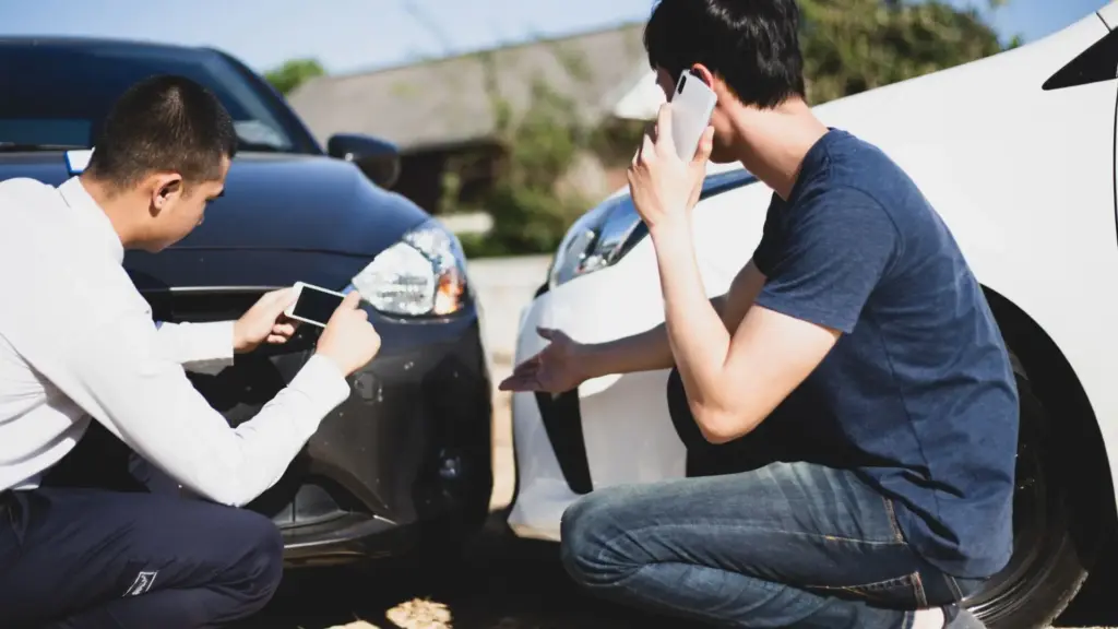 Two people taking pictures of a car crash.