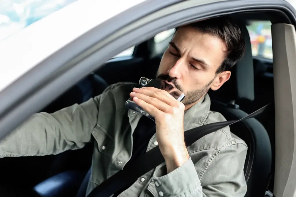A man drinking a flask while behind the wheel. 