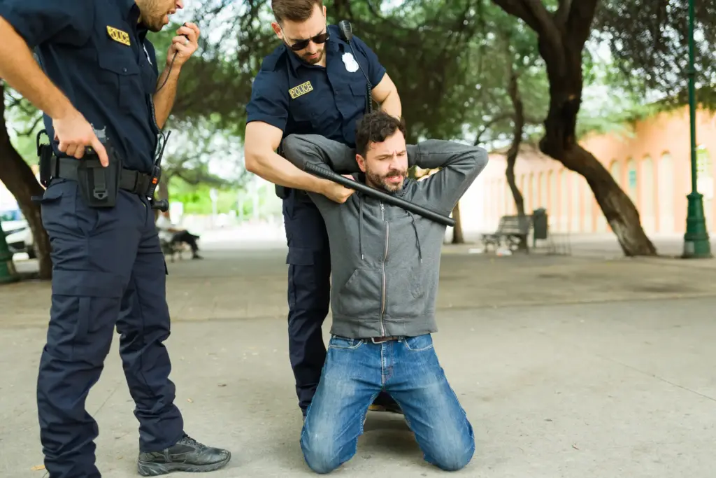 A police officer arresting a man while putting a baton up to his neck.