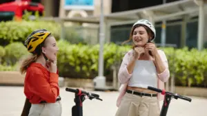 Two women putting on helmets before they ride an electric scooter.