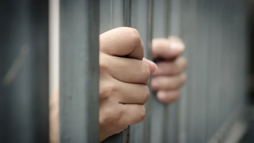 A prisoner holding onto a jail bars.