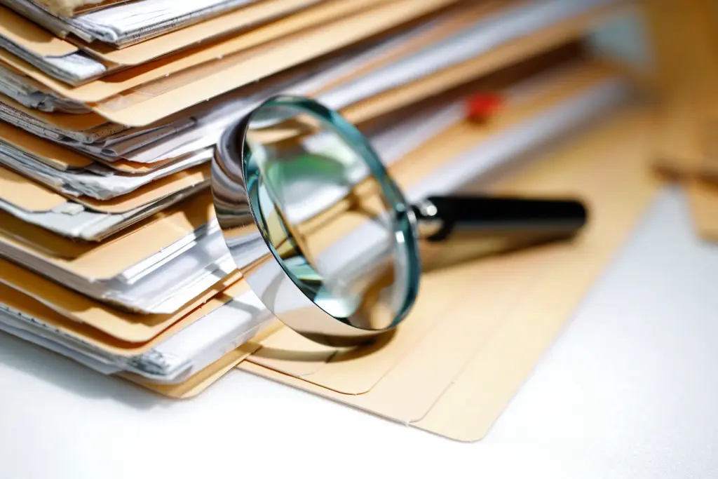 A stack of folders with a magnifying glass in front.