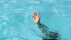 A person drowning in a pool and a person is reaching out for help.