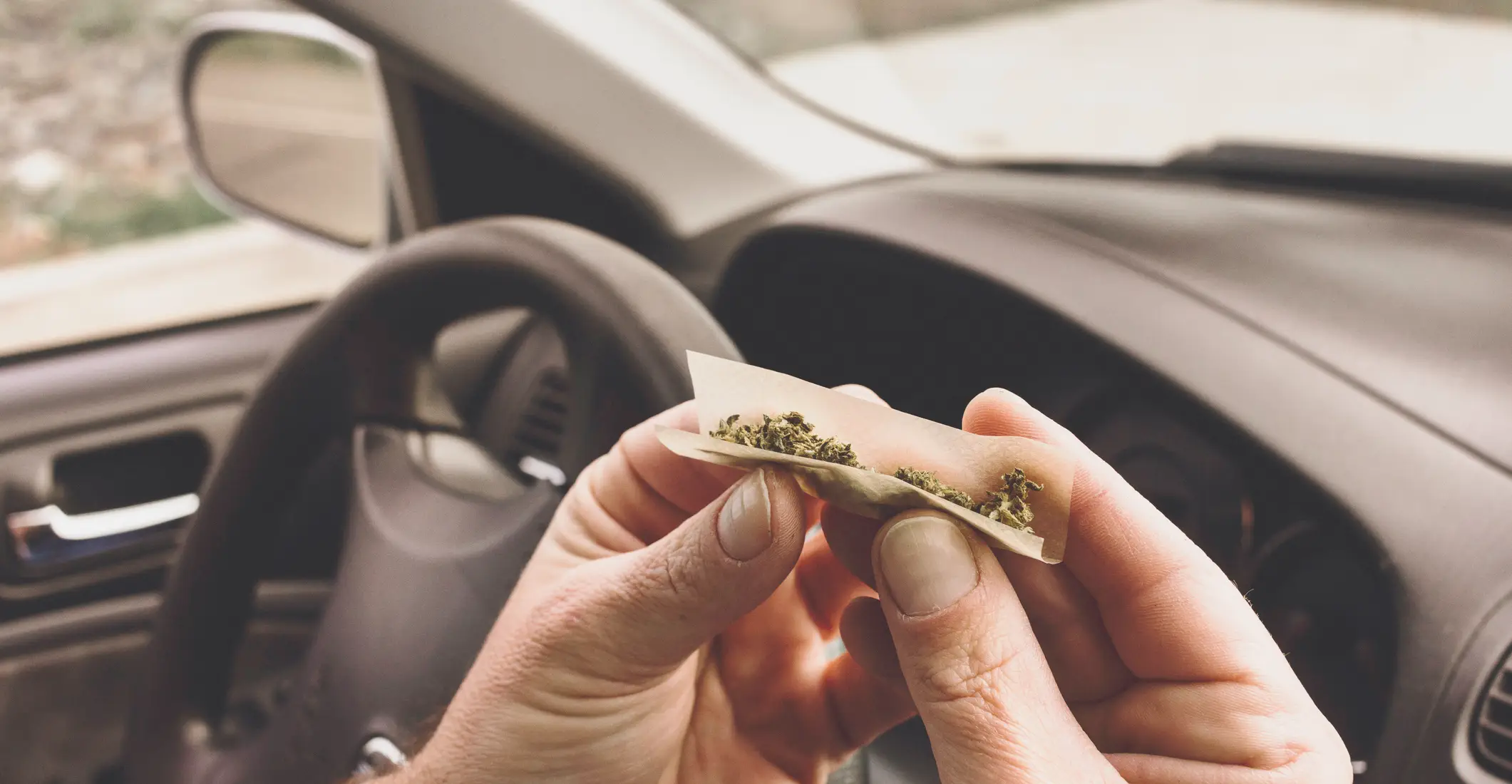 A rolling up a joint in his car.