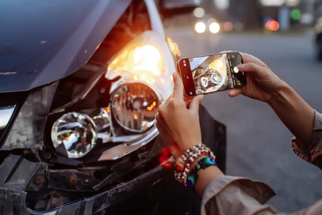 A person taking photos of a busted headlight after a car accident.