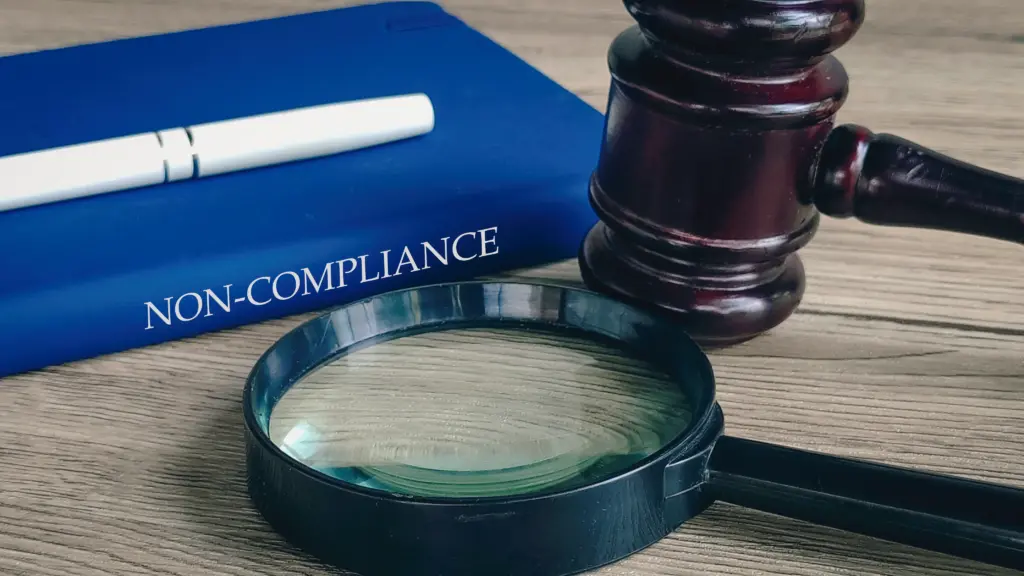 A book titled non-compliance with a pen, a magnifying glass, and a gavel.