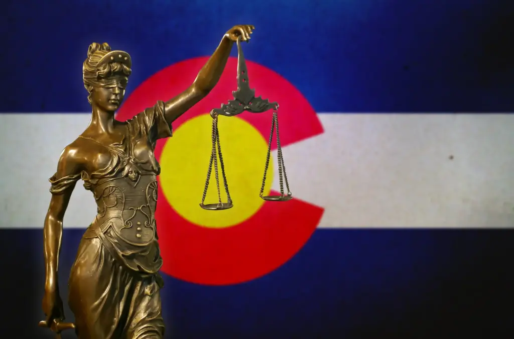 A statue of Lady Justice in front of the Colorado state flag.