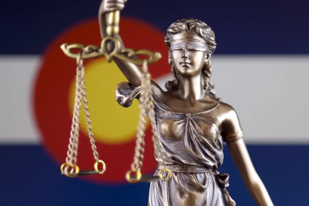 A statue of Lady Justice in front of the Colorado State flag.