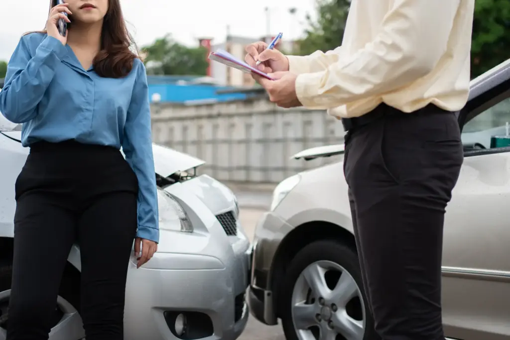 A woman on the phone while an insurance adjuster is writing something down.