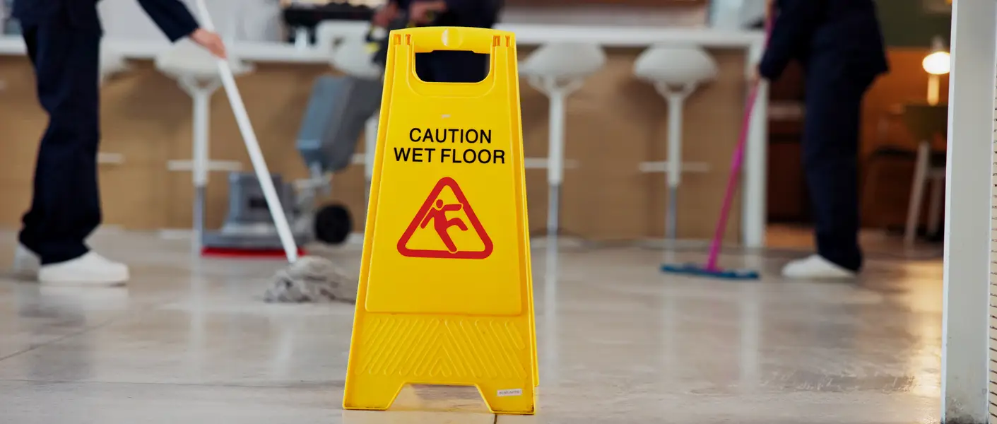 A wet floor sign with people mopping wet floors behind it.