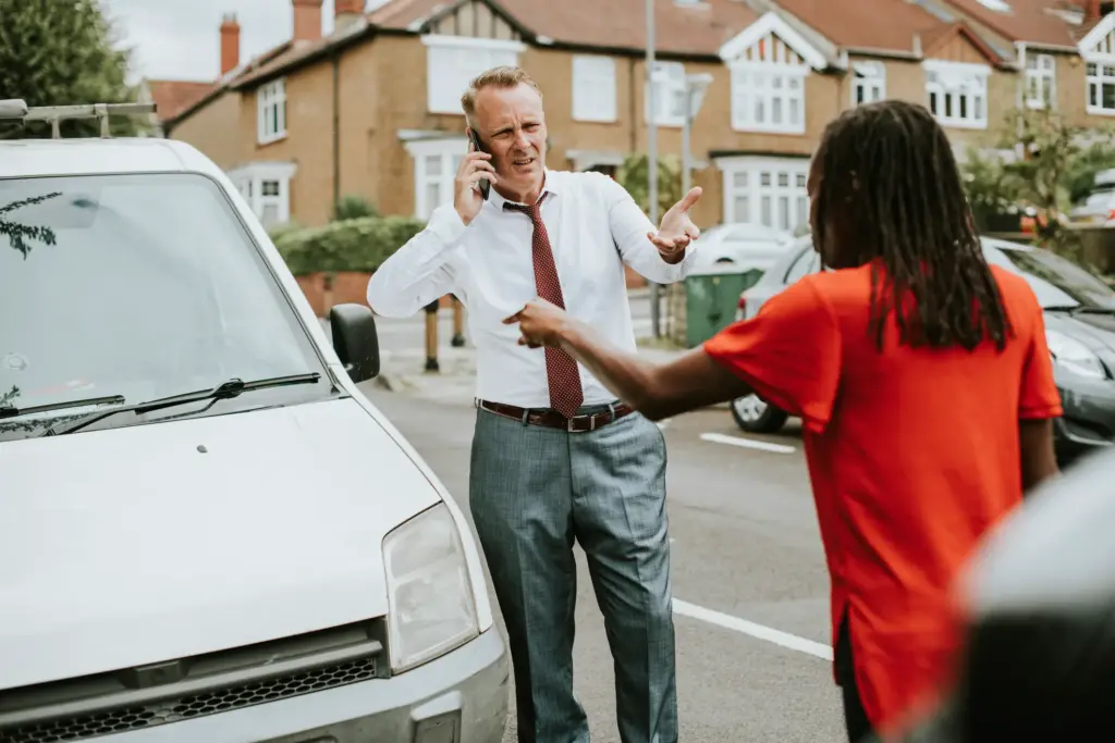 A man on the phone after getting into a car accident with another driver.