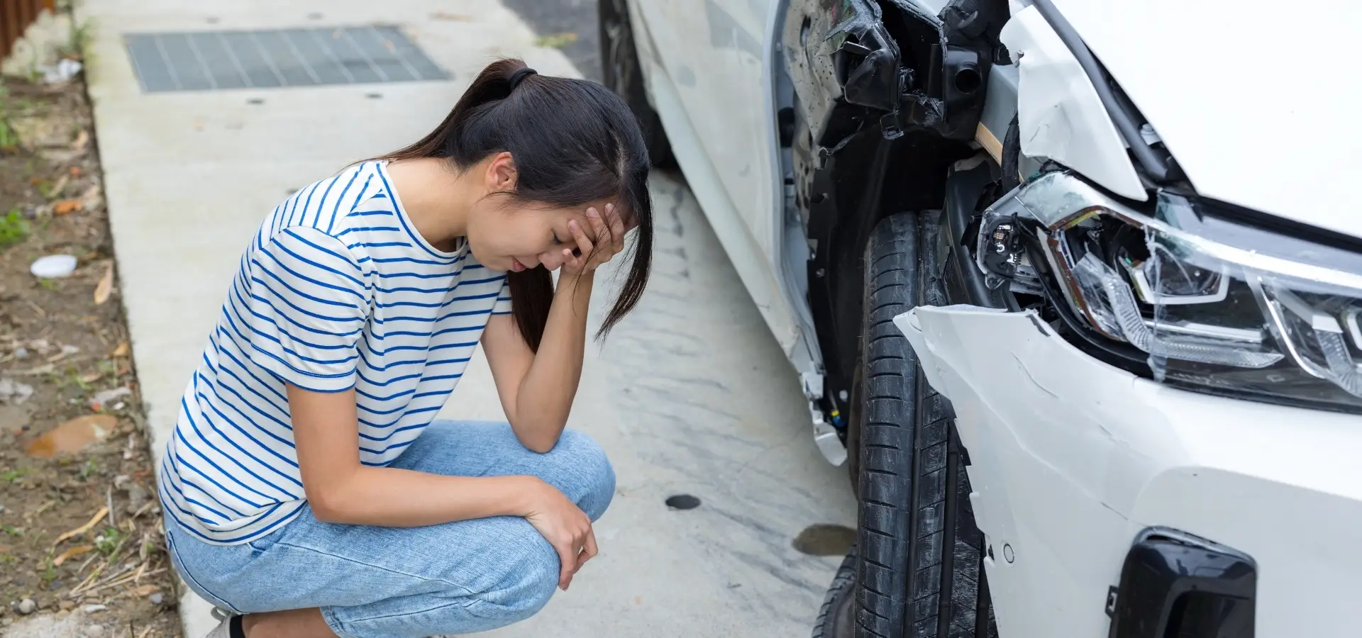A woman looking distressed after seeing damage to her car.